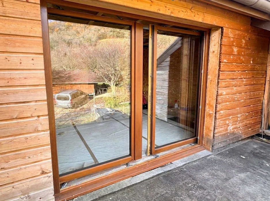 Façade extérieure d'un chalet en bois avec pose de baie vitrée coulissante à deux vantaux, cadre PVC couleur chêne doré