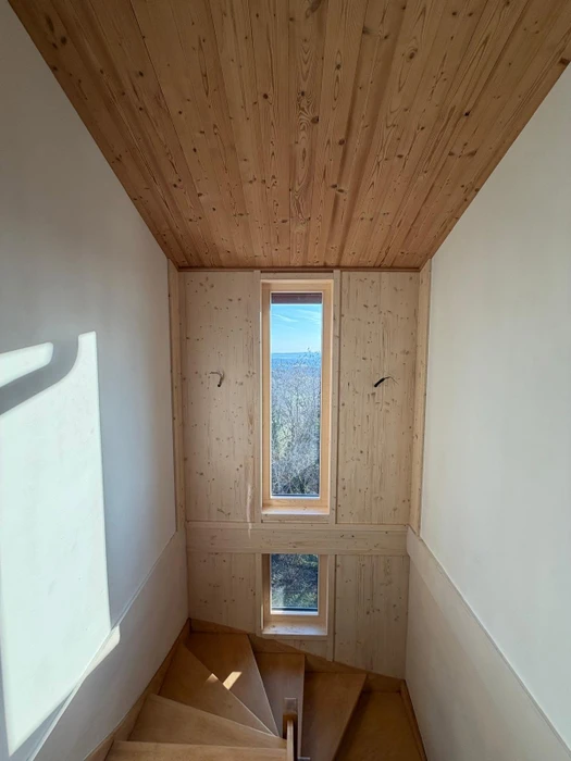 Vue intérieure d'un bâtiment en construction à ossature bois, avec fenêtres coulissantes grand format à cadre pin naturel