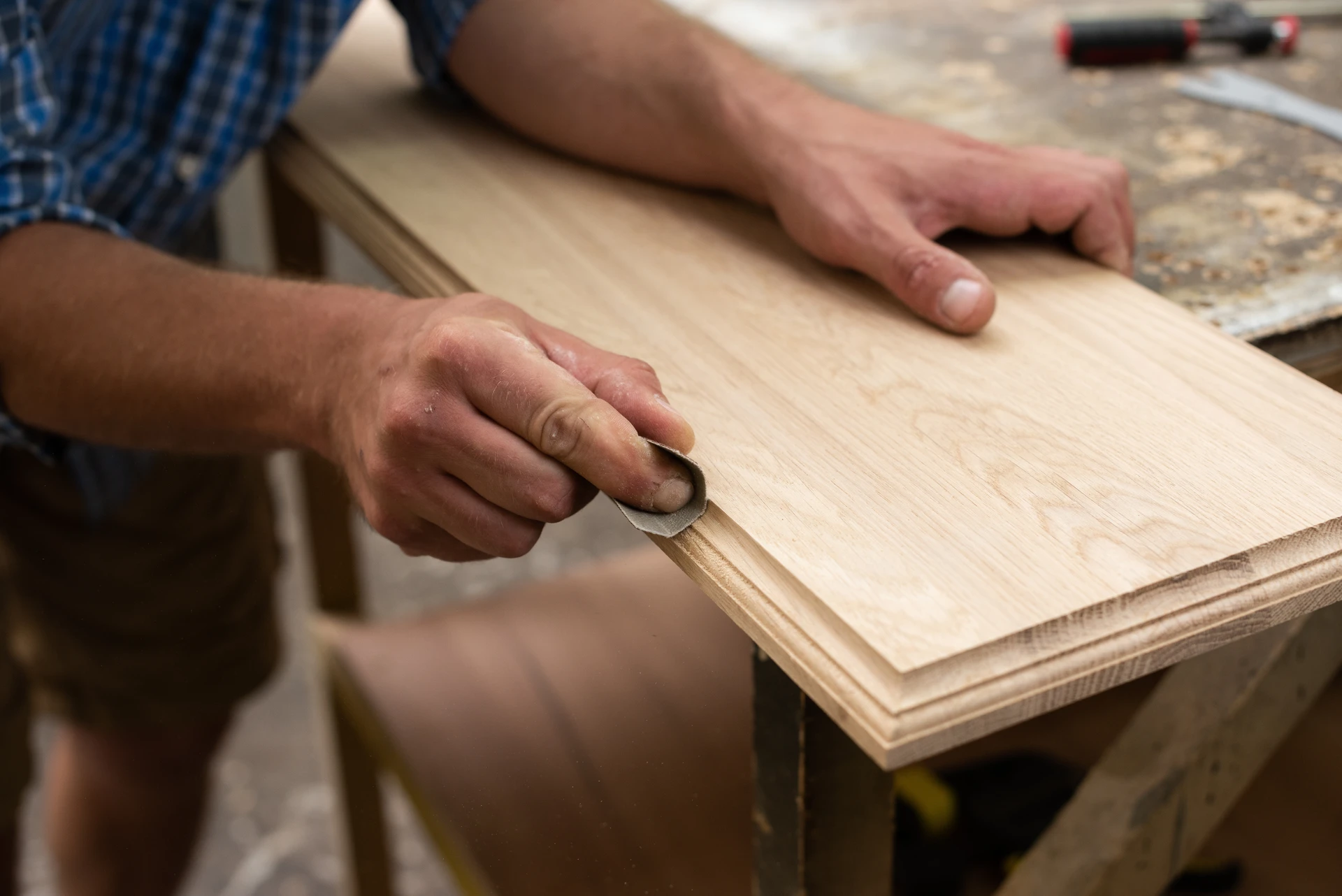 Atelier de menuiserie intérieur, artisan travaillant sur une porte intérieure en pin massif vieilli aux planches horizontales, teinte brun doré avec poignée en métal noir mate et charnières acier apparentes visibles, machines à bois en arrière-plan flou.