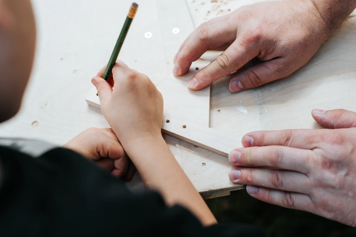 Père et fils travaillent ensemble dans un atelier de menuiserie, mesurant et marquant une planche en bois avec un crayon
